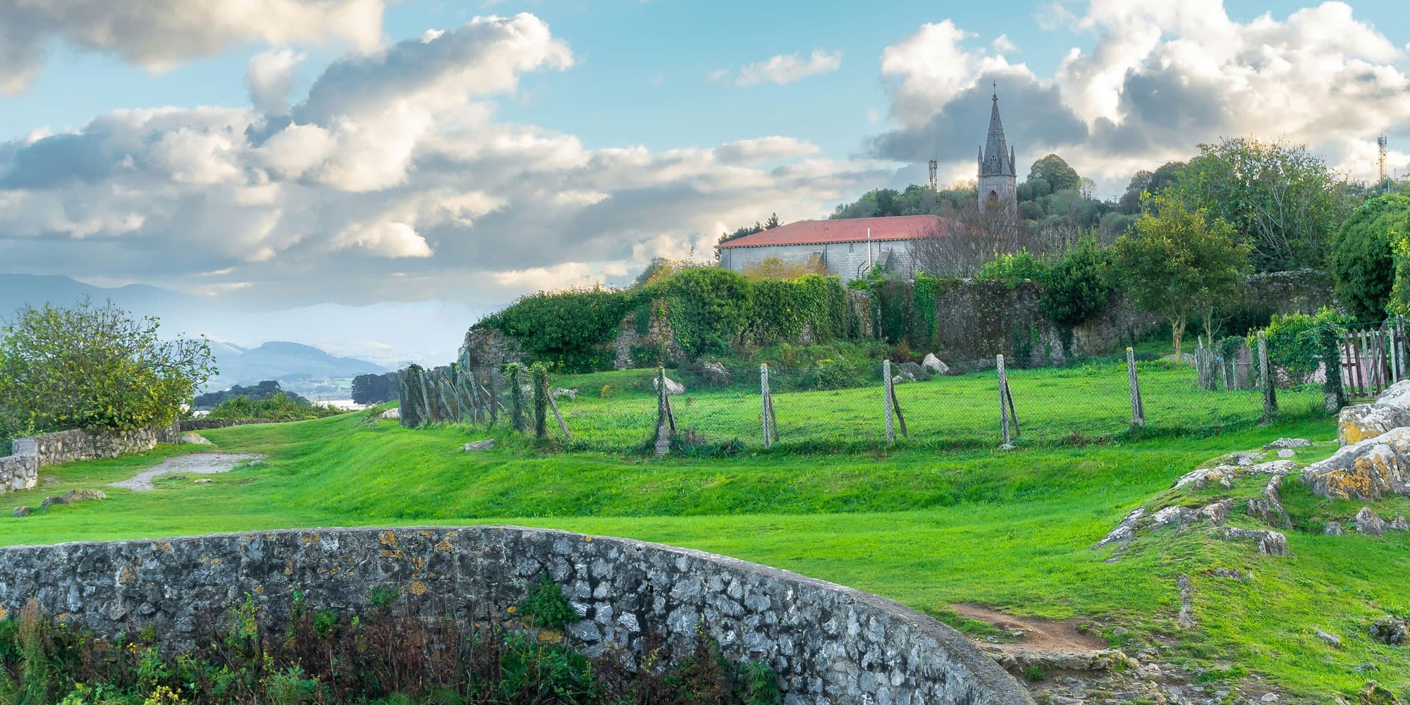 Rural Basque Country landscape with historic church, stone bridge, and greenery.