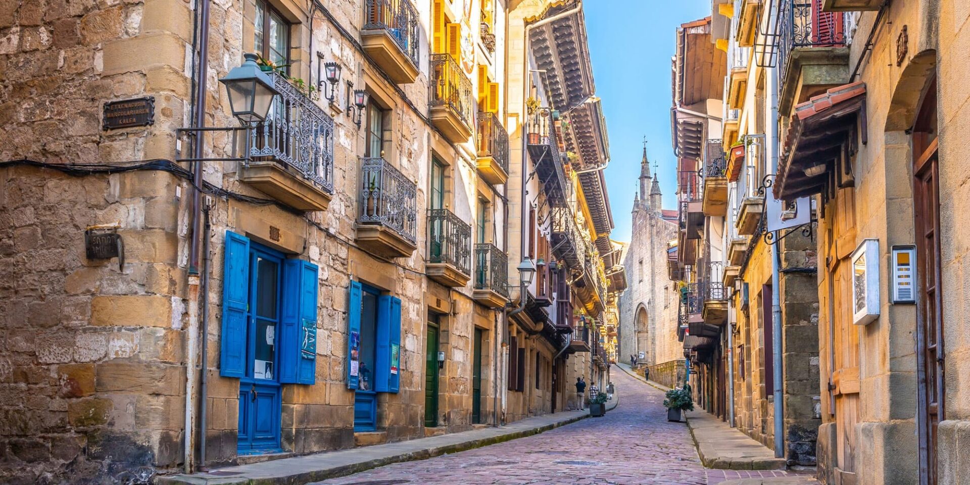 Narrow historic street in Hondarribia with colorful buildings and church spire.