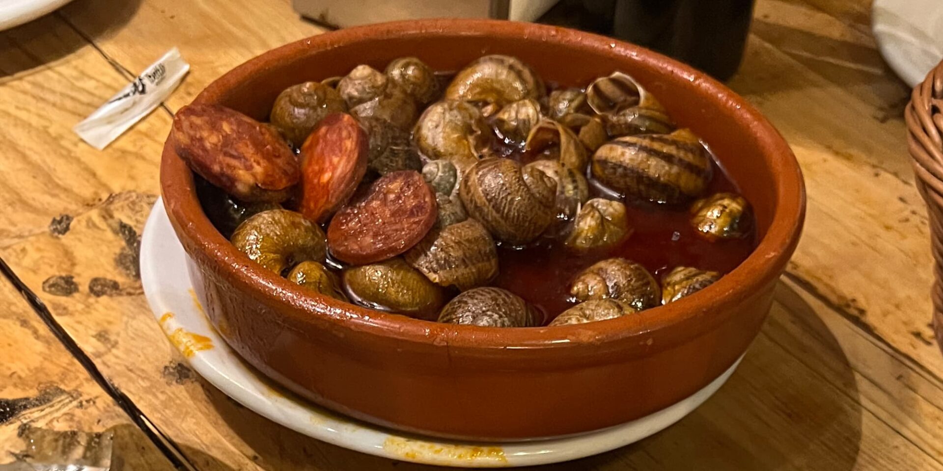 a small dish of snails and chorizo on a wooden table