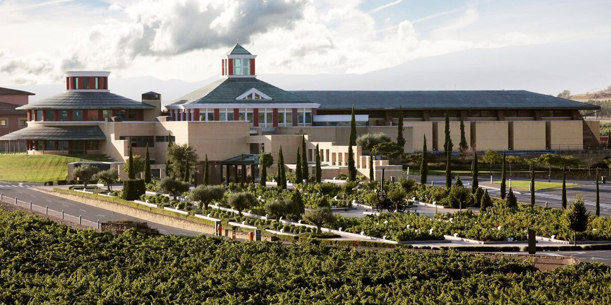 Vivanco wine museum amidst vineyards with mountain backdrop.